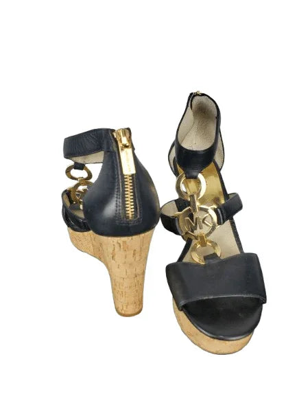 Black wedge sandals with cork sole and gold accents on a white background