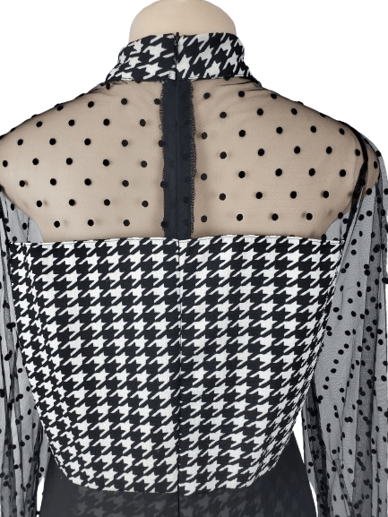 Black and white checkered jumpsuit with sheer sleeves on a mannequin against a white background