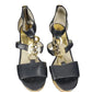 Pair of black high-heeled sandals with gold accents on a white background