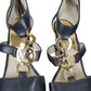 Black high-heeled shoes with gold 'MK' logo on a white background