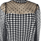 Black and white checkered jumpsuit with sheer sleeves on a mannequin against a white background