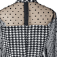 Black and white checkered jumpsuit with sheer sleeves on a mannequin against a white background