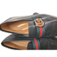 Black leather loafers with a Gucci logo and web strap on a white background