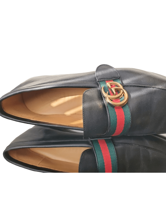 Black leather loafers with a Gucci logo and web strap on a white background