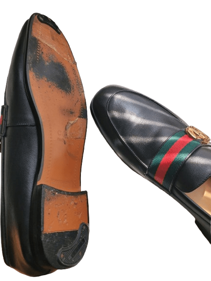 Black leather loafer with a gold buckle and red and green striped strap on a white background