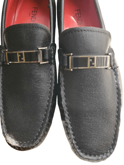 Black loafers with gold logo detail on a white background