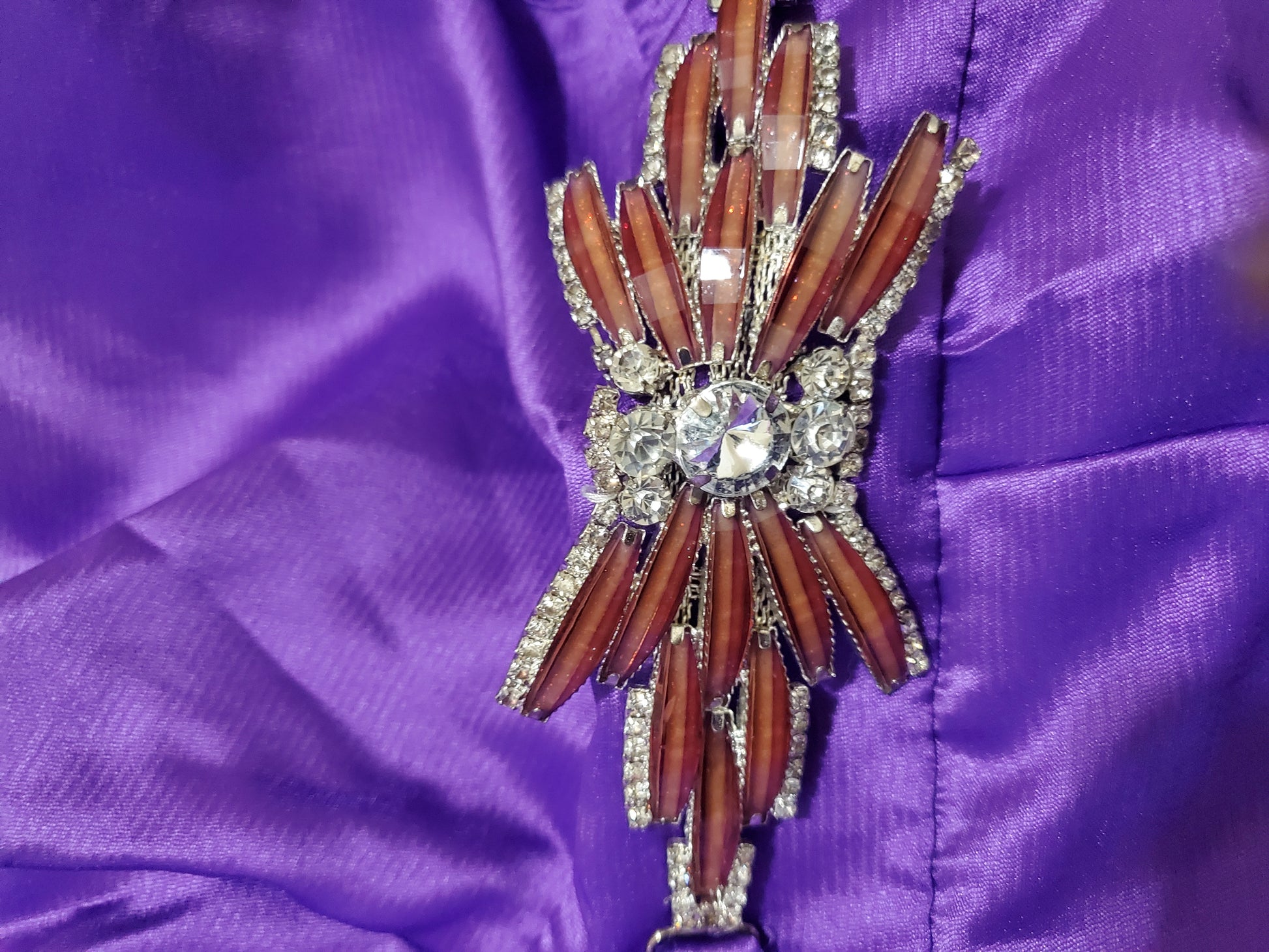 Decorative brooch with wooden-like design and rhinestones on a purple fabric background