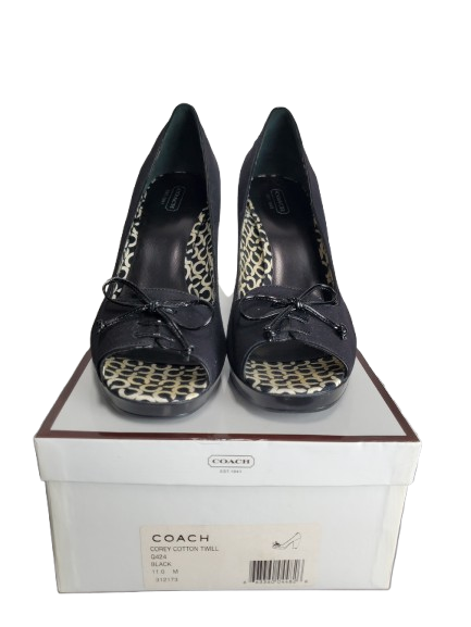 Black high-heeled shoes with leopard print details on a white box labeled 'Coach'.