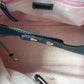 Close-up of a pink bag with a black strap and gold hardware.