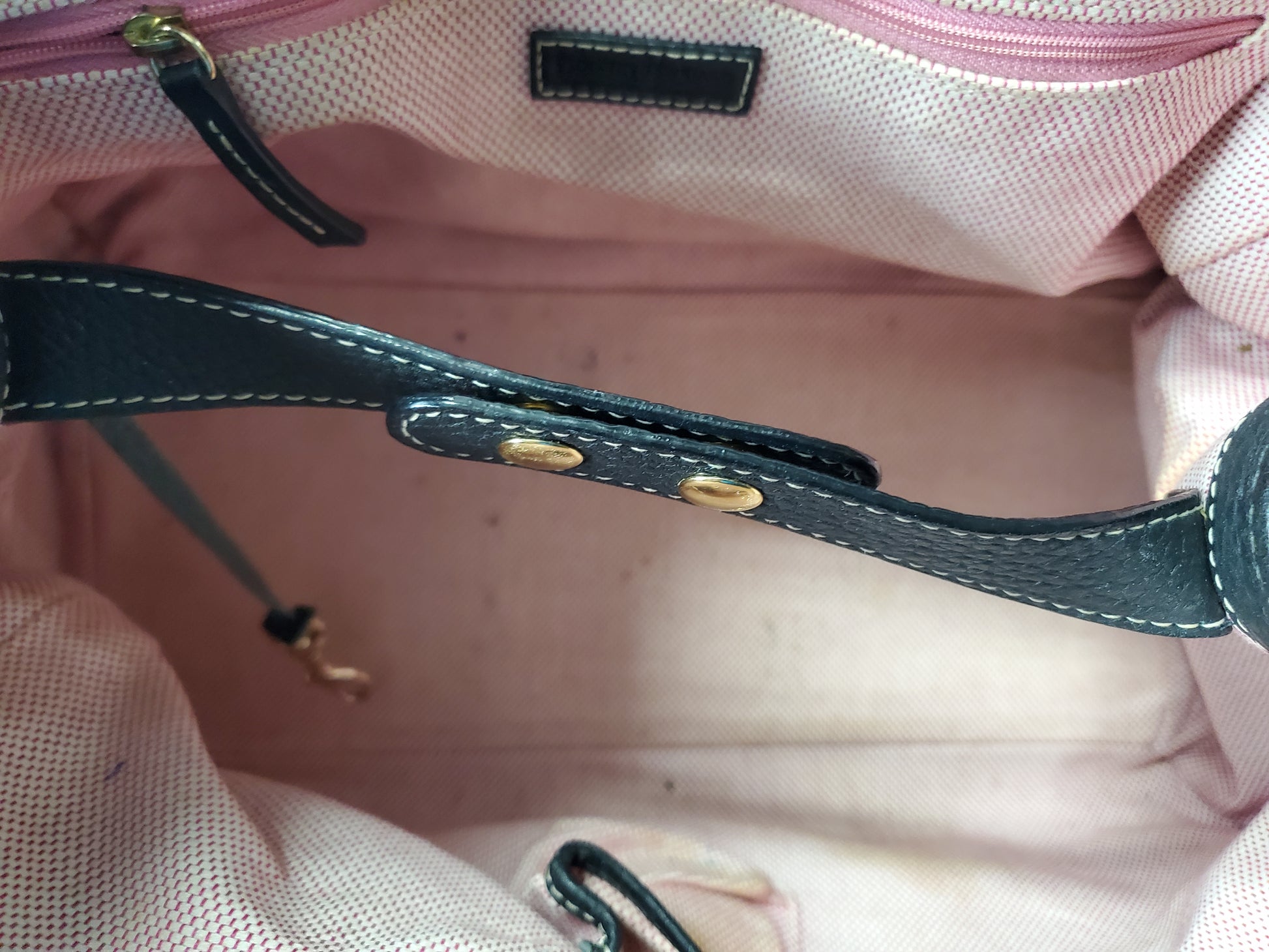 Close-up of a pink bag with a black strap and gold hardware.
