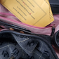 Close-up of a black leather bag with visible branding, pink zipper, and yellow tag.