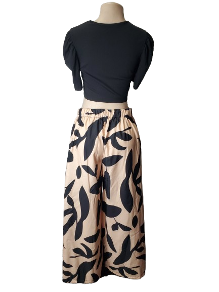 Mannequin wearing a black top and beige pants with black leaf pattern on a white background