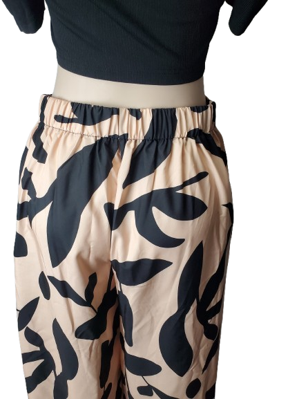 Beige pants with black leaf pattern worn by a person on a white background