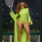 Person in a bright green outfit holding a tennis racket on a tennis court with tennis balls scattered around.